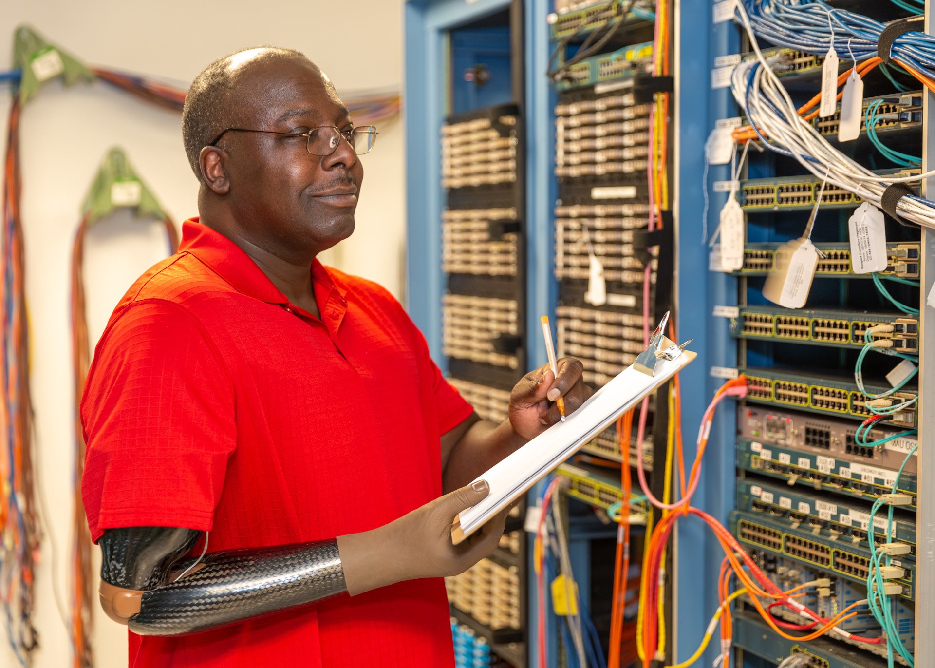 A shoulder disarticulation patient uses his electrically-powered elbow and hand to take notes at work as a server technician.