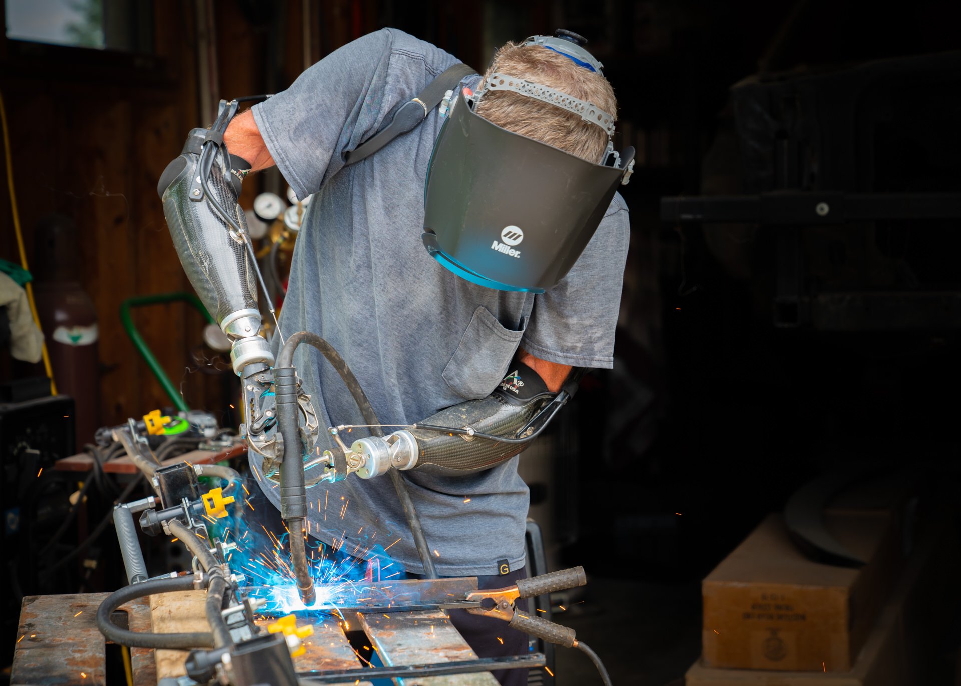 A bilateral transradial patient uses his body-powered prostheses to weld in his shop.