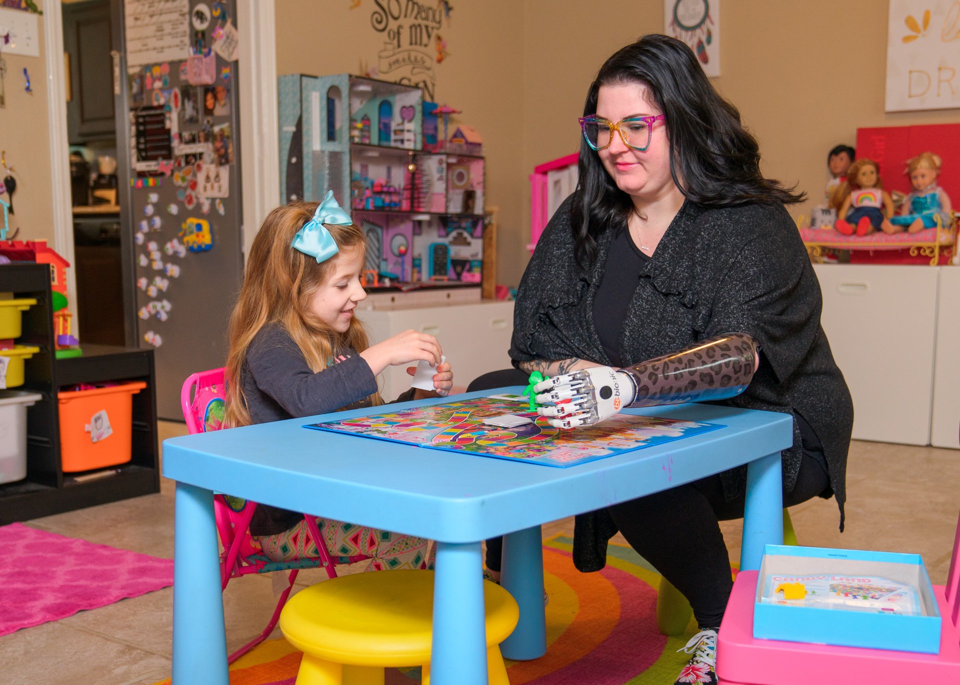 A mother uses her myoelectric hand to play a game of Life with her daughter.