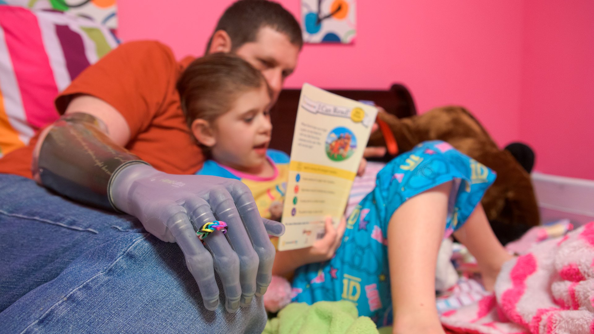 Jason Koger reads a bedtime book with his daughter Cambell while wearing his i-limb prosthesis decorated be her.