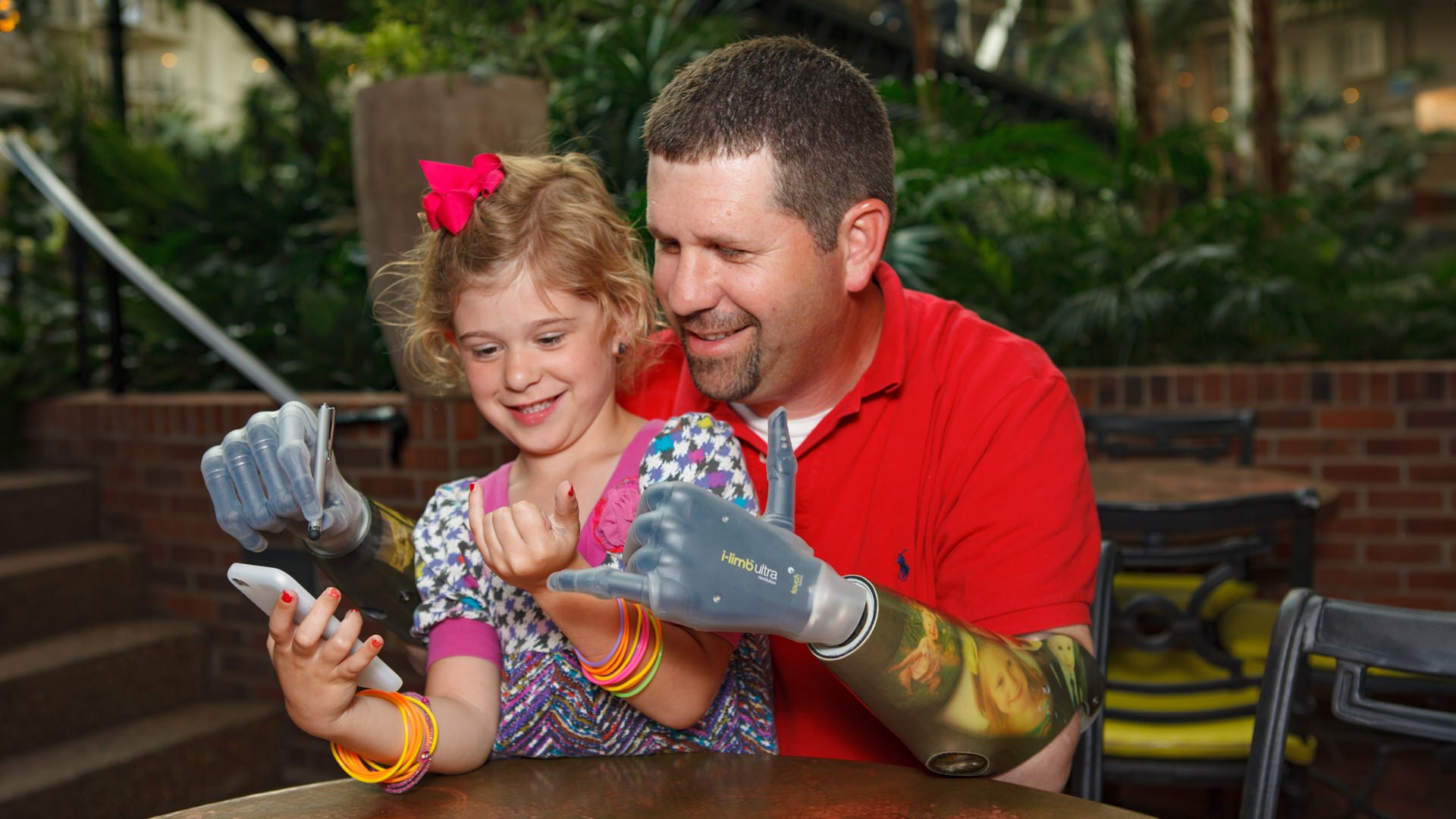 Jason playing a game on his phone with his daughter Cambell using his myoelectric prostheses.